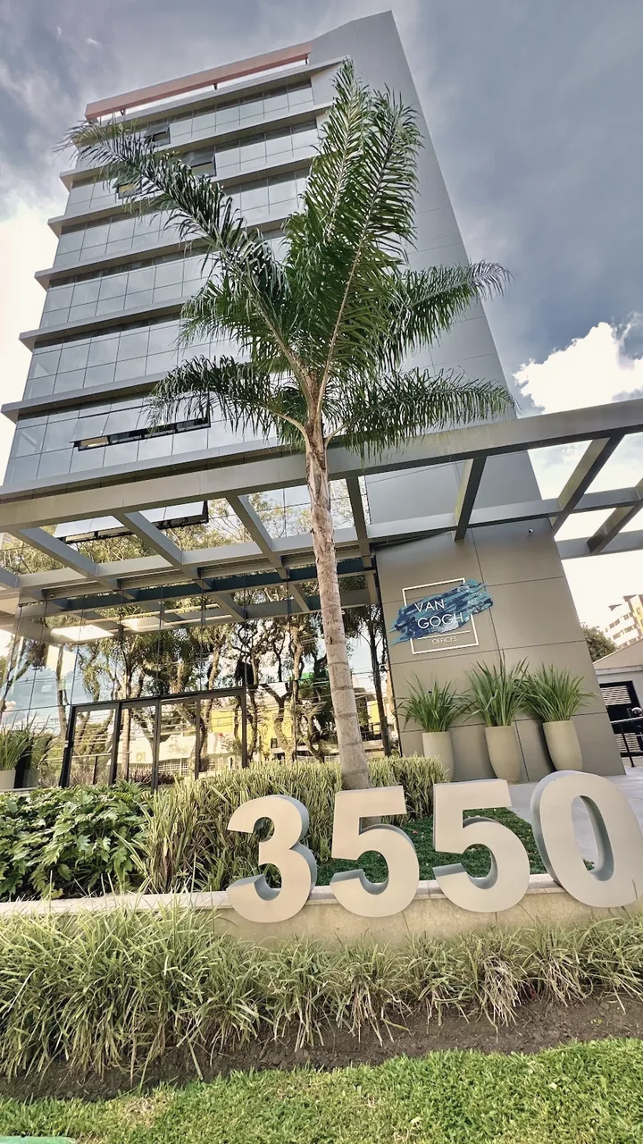 Fachada de vidro do prédio Van Gogh Offices, com palmeiras e o número 3550 no jardim
