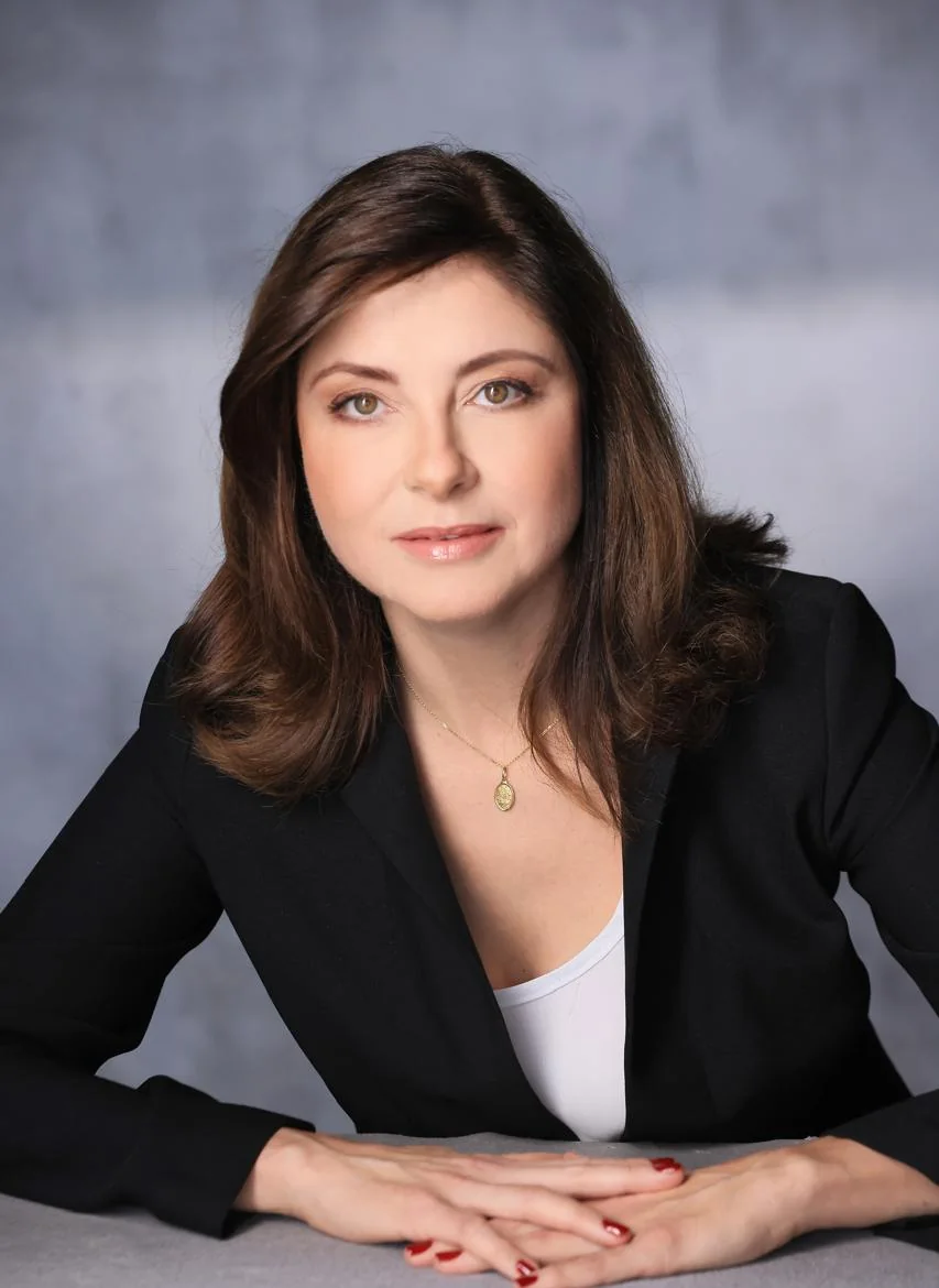 Dra. Vanessa Romanel de blazer preto, com as mãos apoiadas sobre a mesa, olhando para a câmera